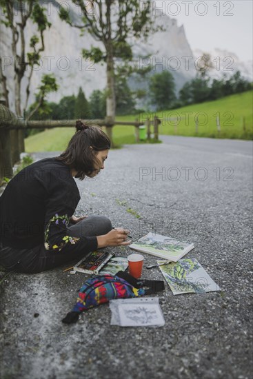 young woman painting mountains on road