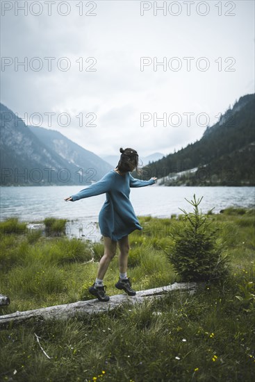 young woman balancing on log by lake