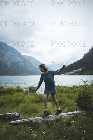 young woman balancing on log by lake