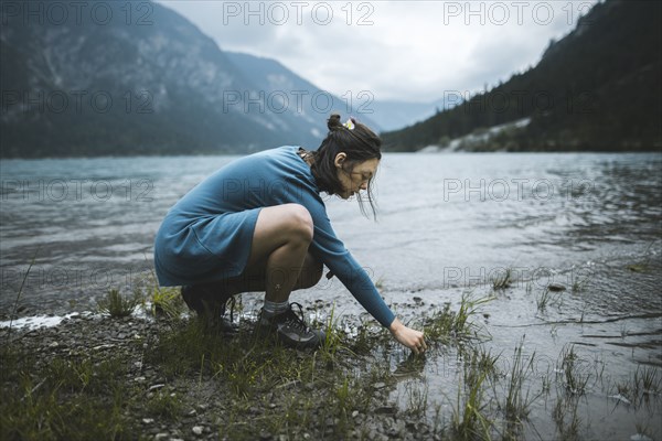 young woman crouching by lake