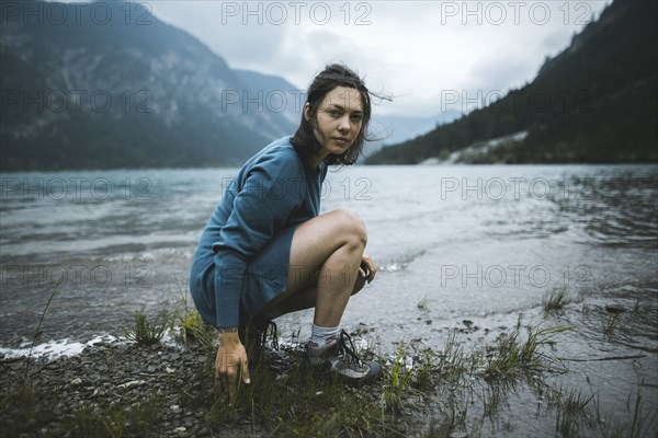 young woman crouching by lake