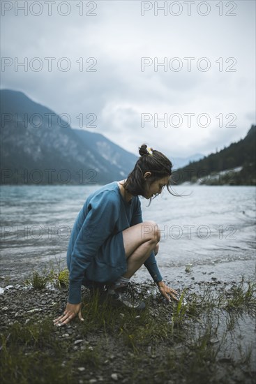 young woman crouching by lake