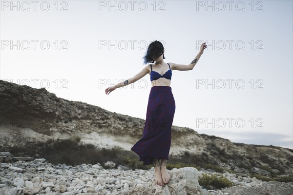 young woman in bra and skirt standing on rock