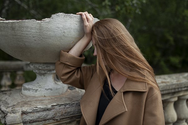 young woman holding broken flower pot on stone banister