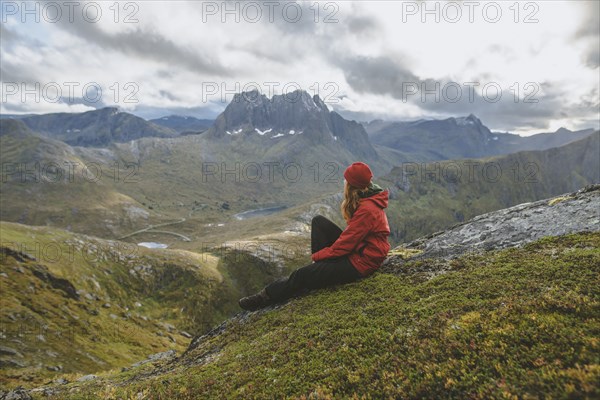 young woman in red jacket sitting on mountain
