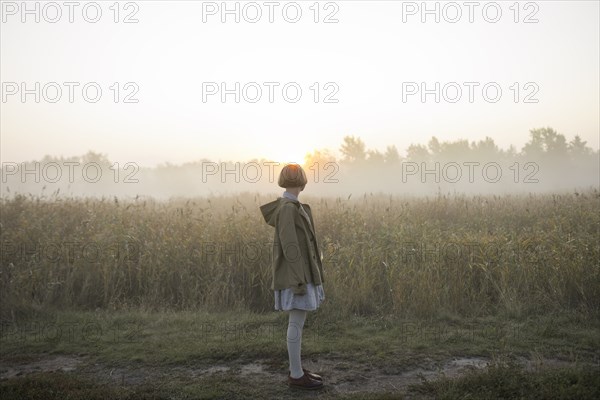 young woman by field of long grass at sunset