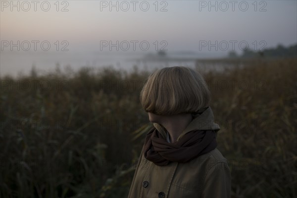 young woman in field by lake at sunset