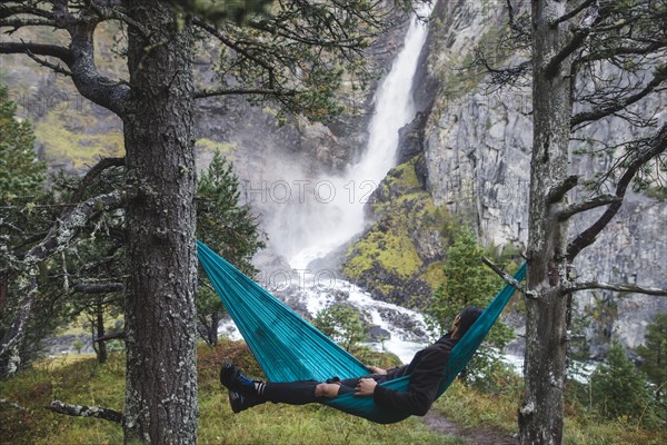 young man resting in hammock by waterfall