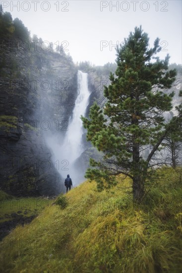 young man standing on hill by waterfall