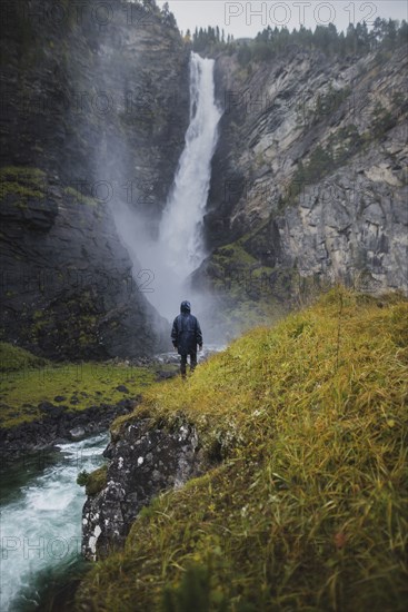 young man standing on hill by waterfall