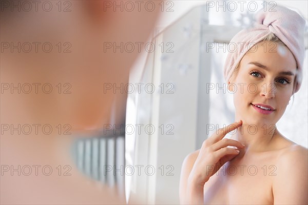Woman wearing towel wrapped around her head looking into mirror
