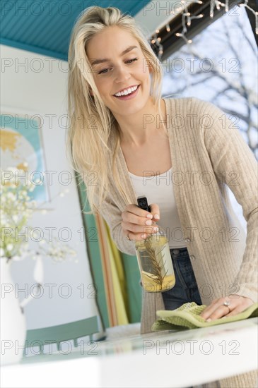 Smiling woman cleaning tabletop with natural cleaning spray