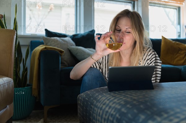 Woman drinking wine and looking at tablet at home