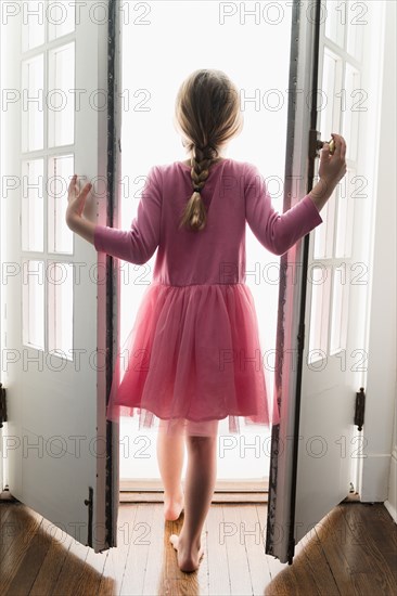 Rear view of girl (6-7) walking through doorway into light