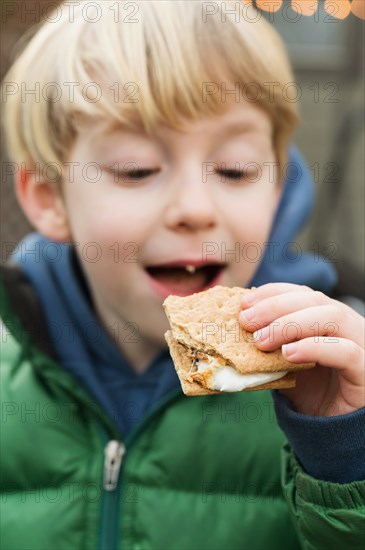 Cute boy (4-5) eating cracker with marshmallow