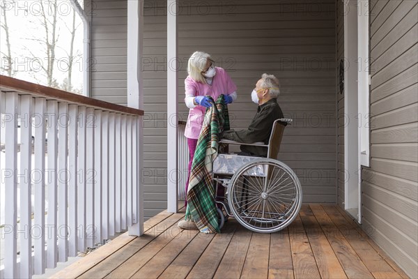 Woman and man in wheelchair wearing protective mask to prevent coronavirus transmission on porch