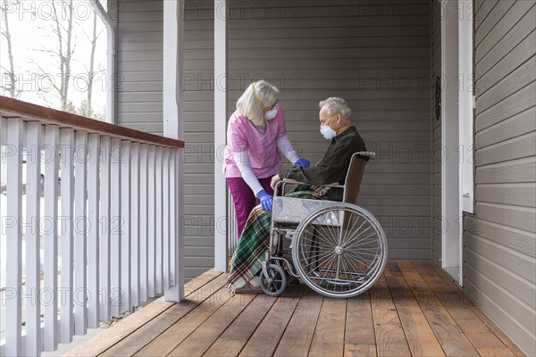 Woman and man in wheelchair wearing protective mask to prevent coronavirus transmission on porch