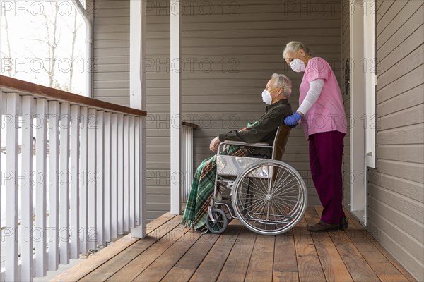 Woman and man in wheelchair wearing protective mask to prevent coronavirus transmission on porch