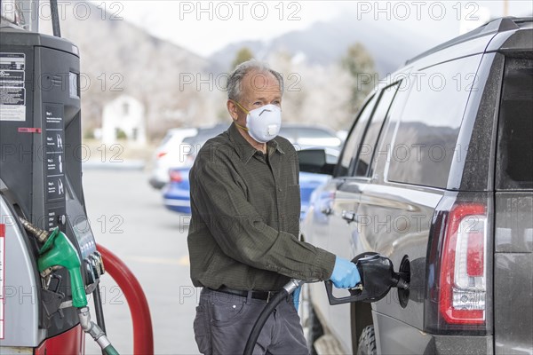 Man wearing surgical gloves and mask refueling car at gas station