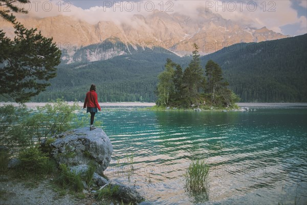 Germany, Bavaria, Eibsee, Young woman standing on rock by Eibsee lake ...