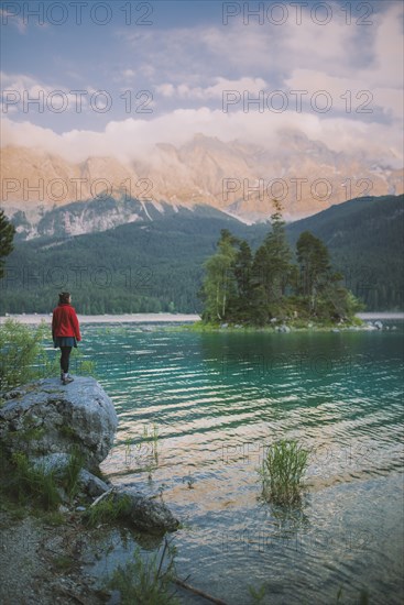 Germany, Bavaria, Eibsee, Young woman standing on rock by Eibsee lake in Bavarian Alps