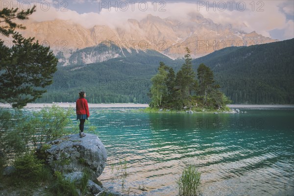 Germany, Bavaria, Eibsee, Young woman standing on rock by Eibsee lake in Bavarian Alps