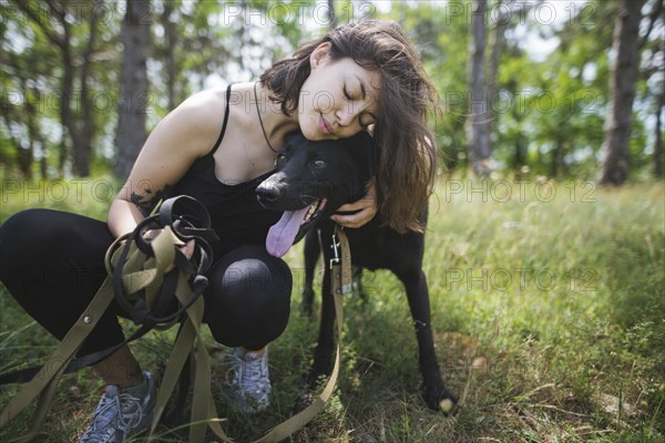 Young woman hugging dog from animal shelter in forest