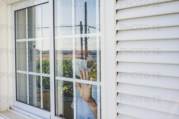 Teenage boy (16-17) wearing protective mask looking through window