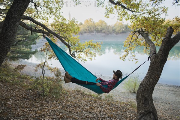 Italy, Man lying in hammock near lake