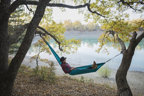 Italy, Man lying in hammock near lake