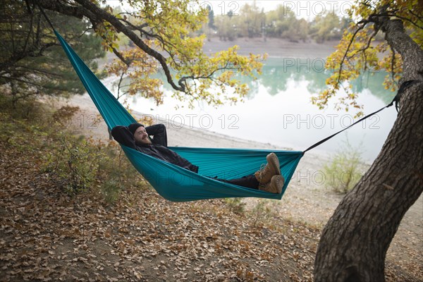 Italy, Smiling man lying in hammock near lake