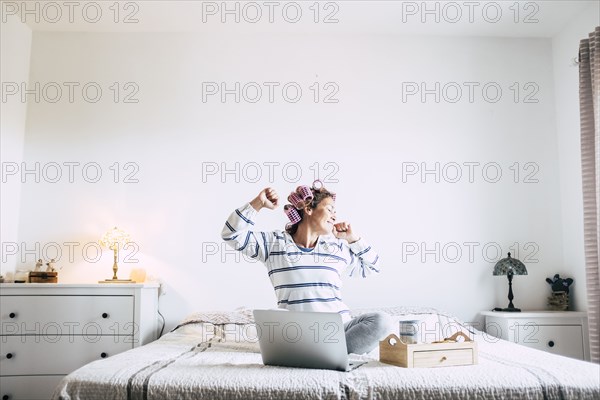 Woman sitting on bed with laptop and stretching
