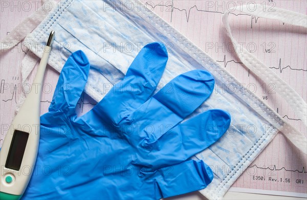 Latex glove, hygiene mask and thermometer on electrocardiogram