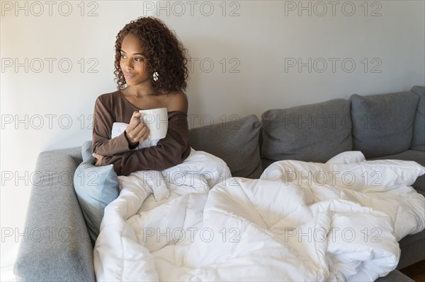 Woman on sofa with cup and blanket