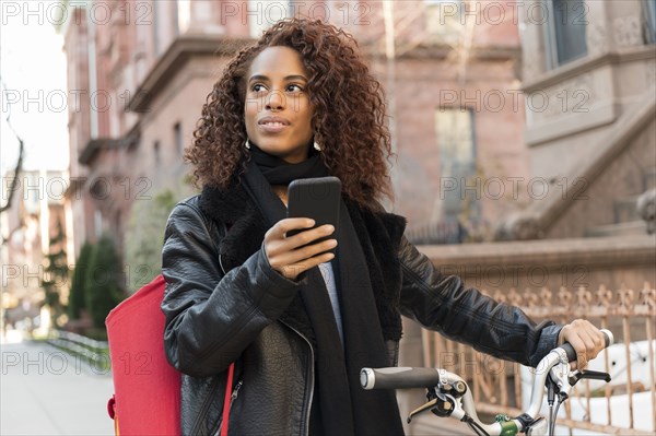 Woman holding smart phone and bicycle in city