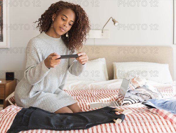 Woman on bed photographing clothes with smart phone