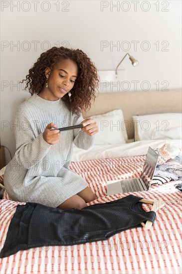 Woman on bed photographing clothes with smart phone