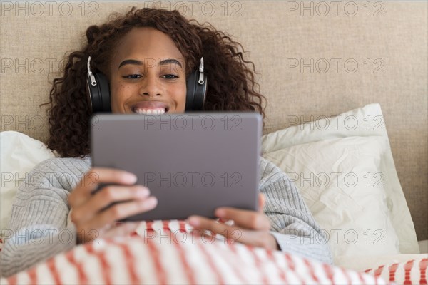 Smiling woman using tablet with headphones in bed