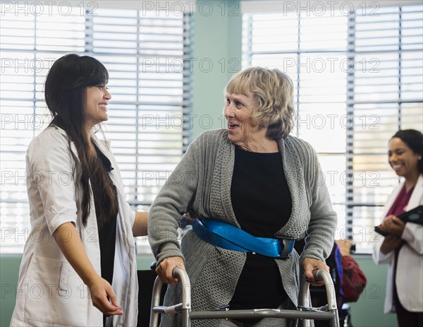 Smiling doctor helping senior woman use walking frame