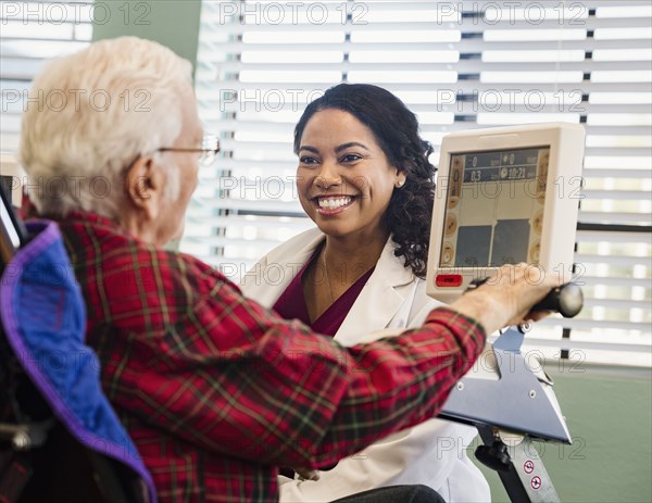 Smiling doctor and senior man by machine monitor