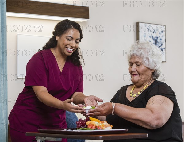 Smiling nurse handing food to senior woman