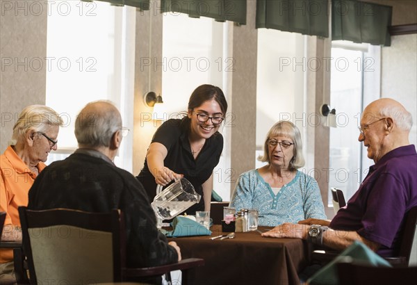 Smiling waitress pouring water for senior people