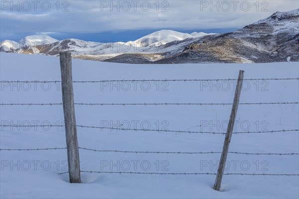 Barbed wire fence in snow with mountains in distance