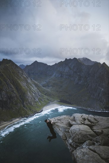 Man hanging on cliff at Ryten mountain in Lofoten Islands, Norway
