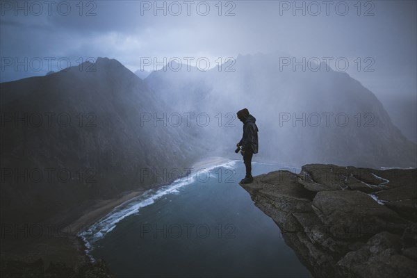 Man holding camera on cliff at Ryten mountain in Lofoten Islands, Norway