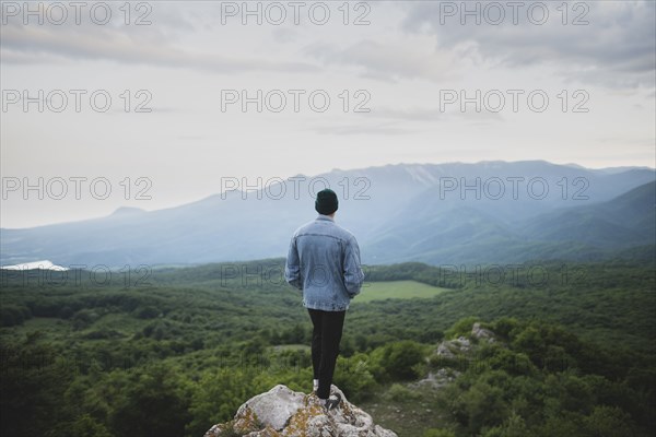 Man standing on cliff by mountain and forest