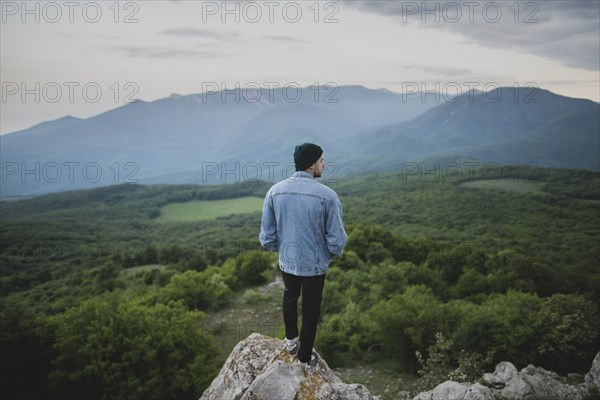 Man standing on cliff by mountain and forest