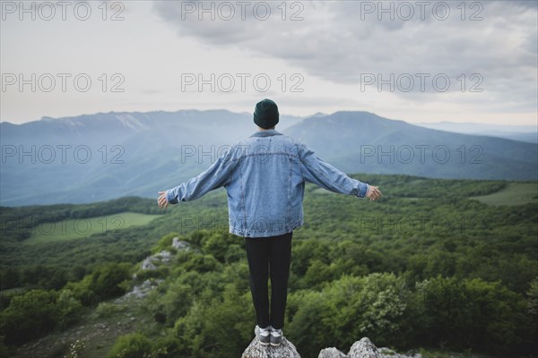 Man standing on cliff by mountain and forest