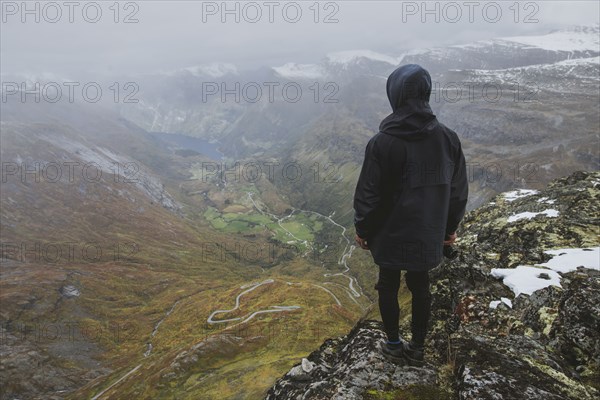 Man holding camera on Dalsnibba mountain overlooking valley in Geiranger, Norway