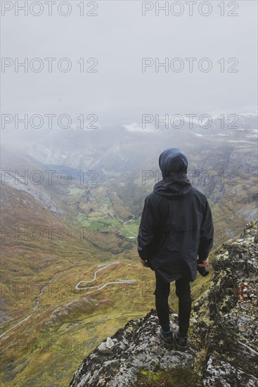 Man holding camera on Dalsnibba mountain overlooking valley in Geiranger, Norway